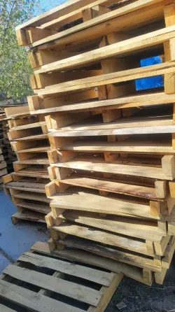 Деревянные поддоны, сложенные штабелями на улице, рядом с другими поддонами