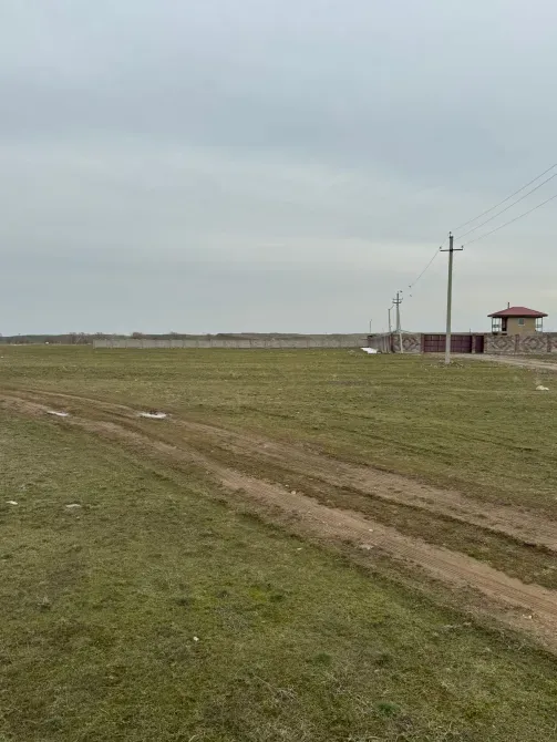 Пейзаж с пустым зелёным полем, линиями электропередач и загородным зданием на горизонте