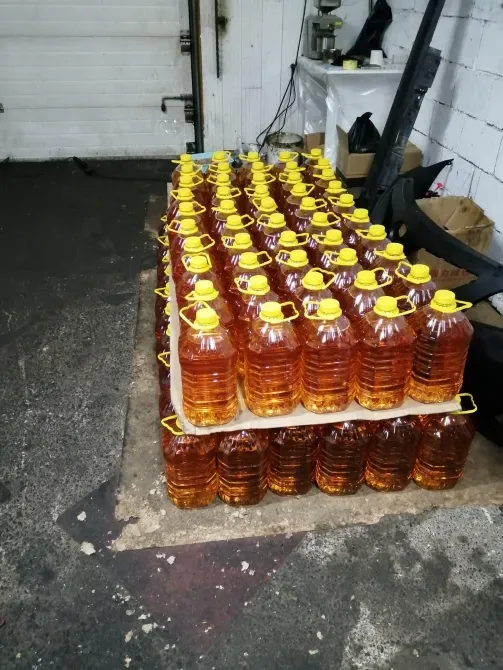 Много бутылей с ярко-желтыми крышками, заполненных жидкостью оранжевого цвета, на поддоне в помещении