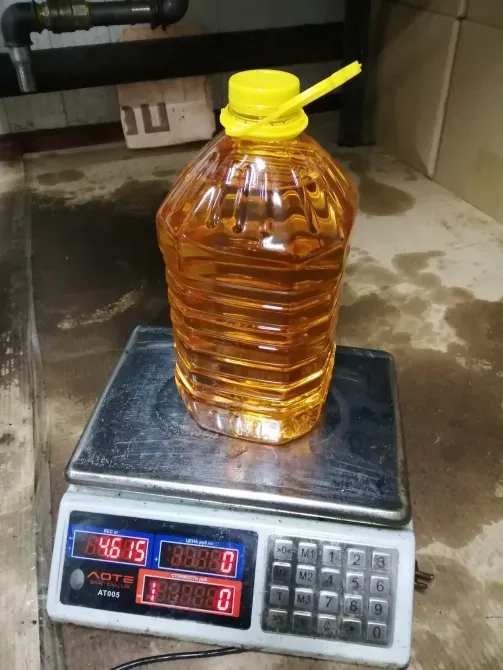 Бутыль с ярко-желтой крышкой, содержащая жидкость оранжевого цвета, стоит на весах