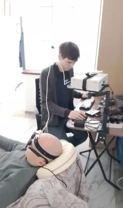 Мужчина работает за компьютером, наблюдая за человеком на кресле с электроникой