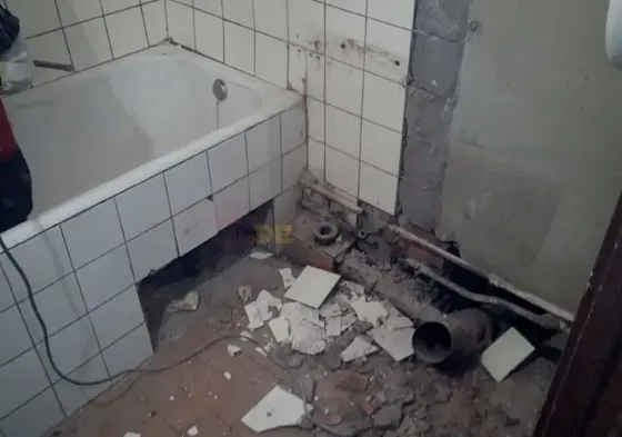 Каска киген жұмысшы бос бөлмедегі қабырғалары бұзылған және құрылыс материалдарымен толы жөндеу процесін бағалауда