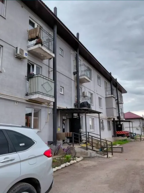 Үй жанындағы автотұрақ және бұлттардың фонында көпқабатты ғимараттар