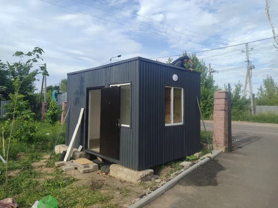 небольшое черное здание с дверью и окнами на фоне неба