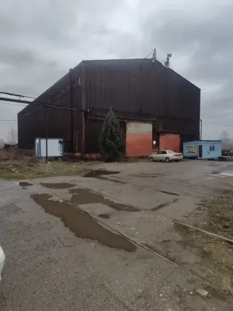 Сұр қабырғалары мен қызыл қақпалары бар өнеркәсіптік ғимарат, бұлтты аспан фонында