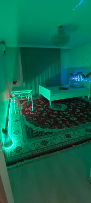 Комната с белой кроватью и зеленым светом, девушка сидит на стуле