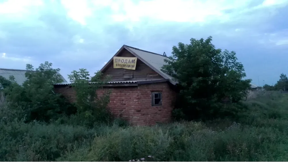 заброшенное строение с надписью о продаже и зарослями