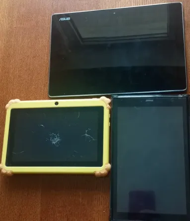 Планшет ASUS и два других устройства, один из которых ярко-желтого цвета с игрушечным улитком, на деревянной поверхности
