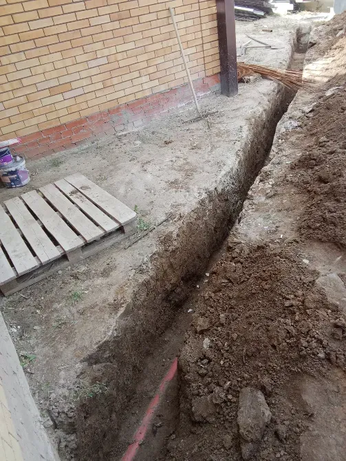 Яма для закладки фундамента рядом с кирпичной стеной