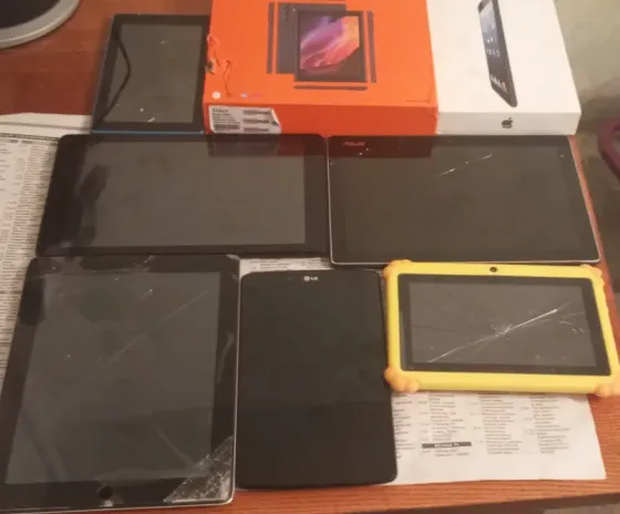 Разнообразие планшетов на деревянном столе: несколько моделей, включая iPad, планшеты LG и ASUS, а также коробки от устройств