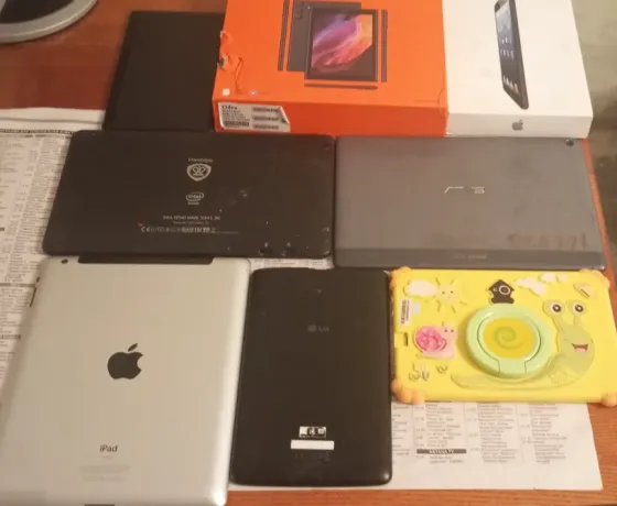 Разнообразие планшетов на деревянном столе: несколько моделей, включая iPad, планшеты LG и ASUS, а также коробки от устройств
