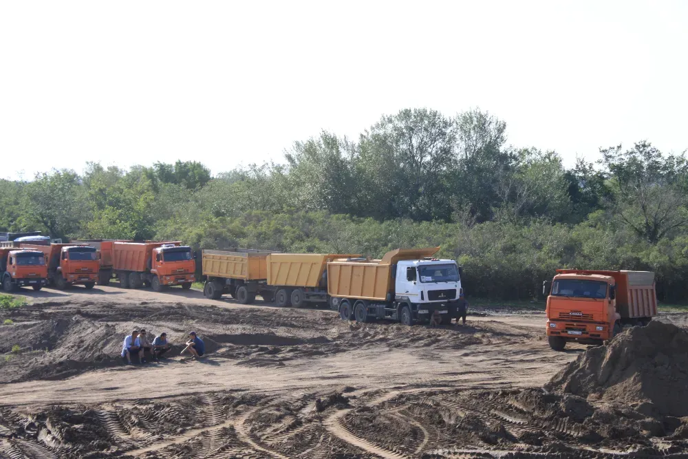 Грузовики на стройплощадке с рабочими на земле